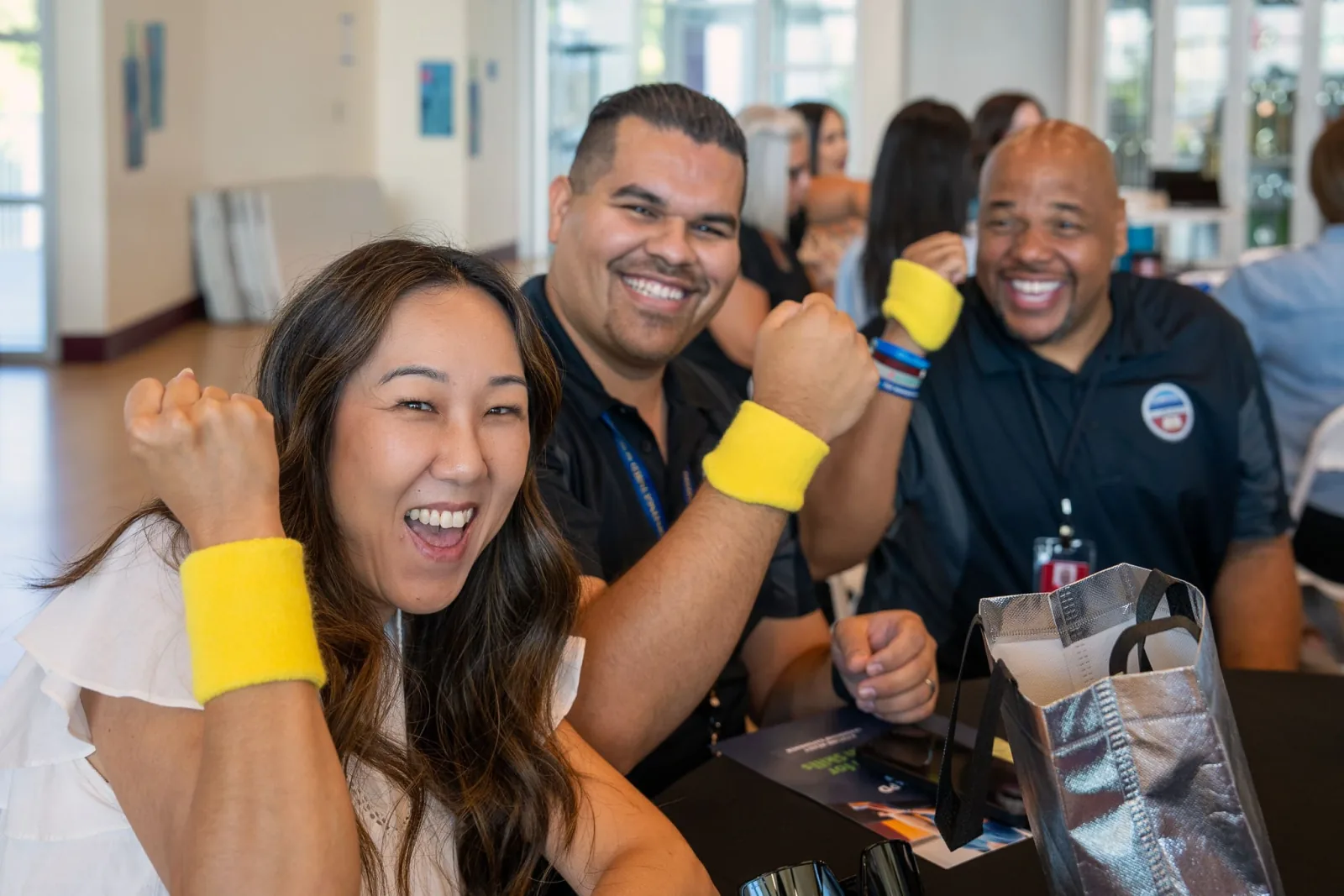 Three educators in yellow wristbands laugh and throw a fist in the air during a session